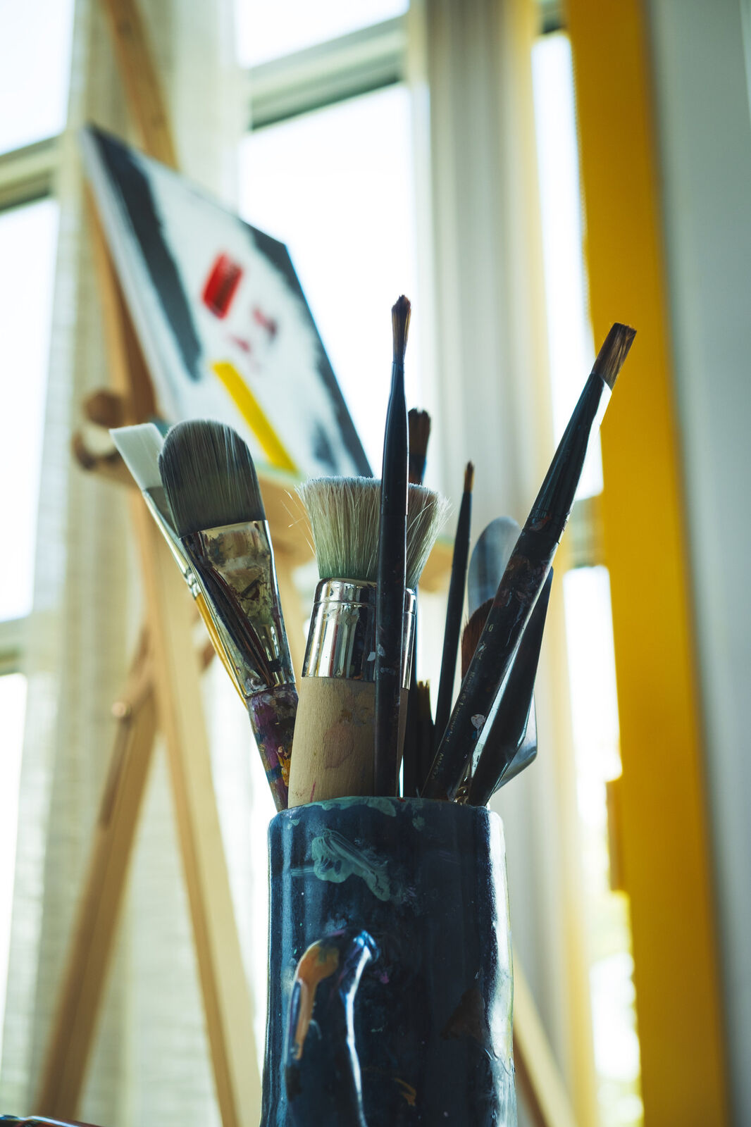 Paintbrushes resting in a jar of water by a sunlit window.