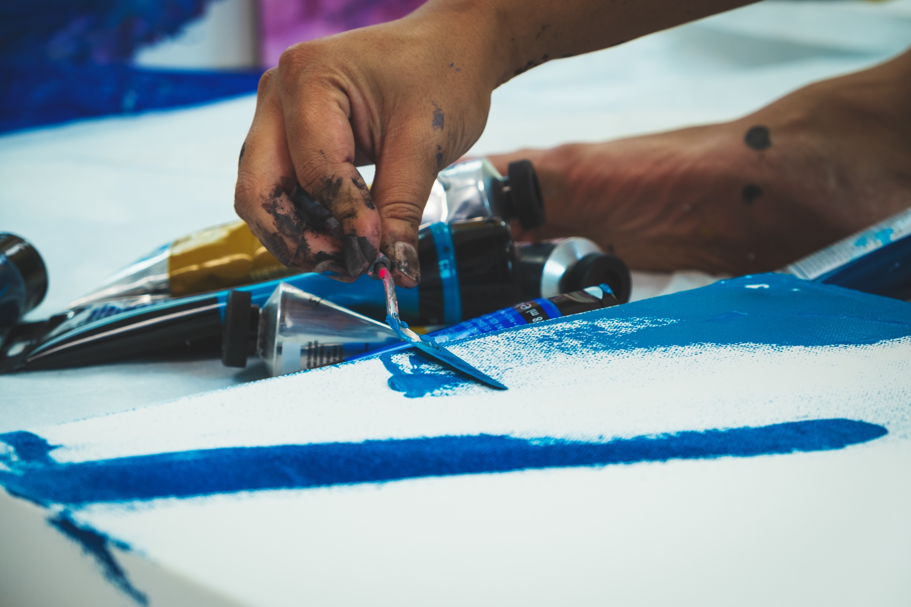 Hands mixing blue paint with a palette knife.